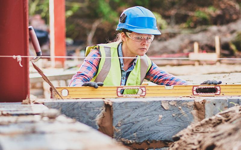 A young female builder using a level to build and check a wall