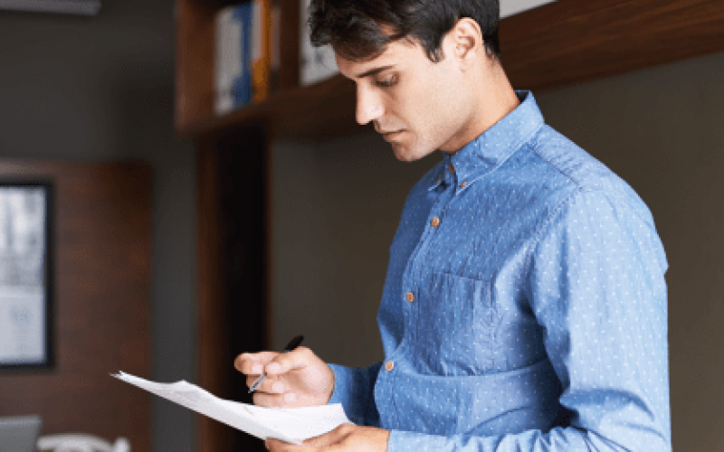 Photograph of a young man in a blue shirt holding pen and paper