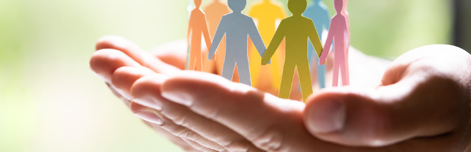 Agos-olwg o ddwy law yn dal yn dyner grŵp o dorluniau papur lliwgar wedi’u siapio fel ffigurau dynol.  