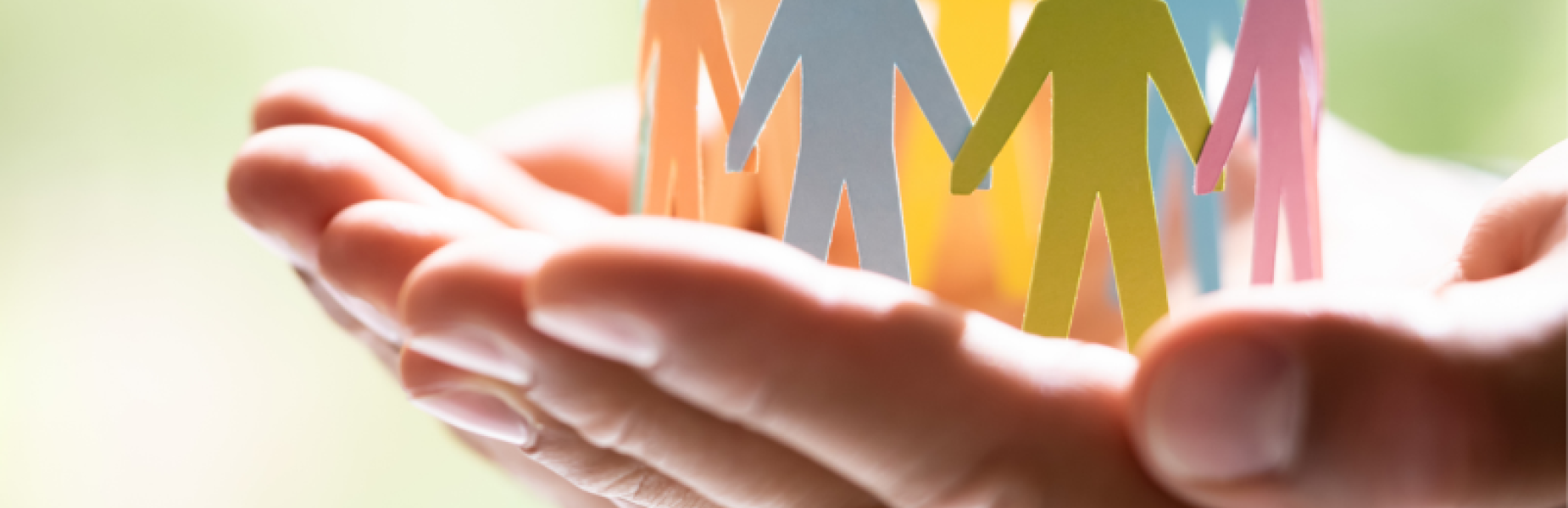Hands gently holding a group of colorful paper cut-out figures standing in a circle.