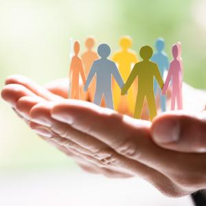 Close-up of two hands gently cupping a group of colorful paper cutouts shaped like human figures.