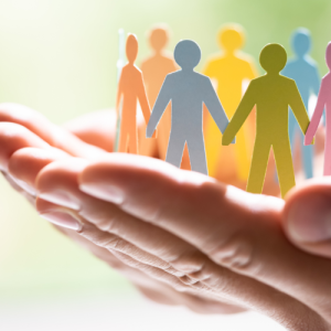 Hands gently holding a group of colorful paper cut-out figures standing in a circle.